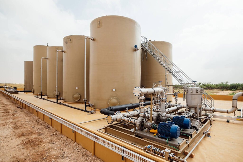 Large water storage tanks with connected piping, pumps, and a metal access stairway at an industrial water facility.